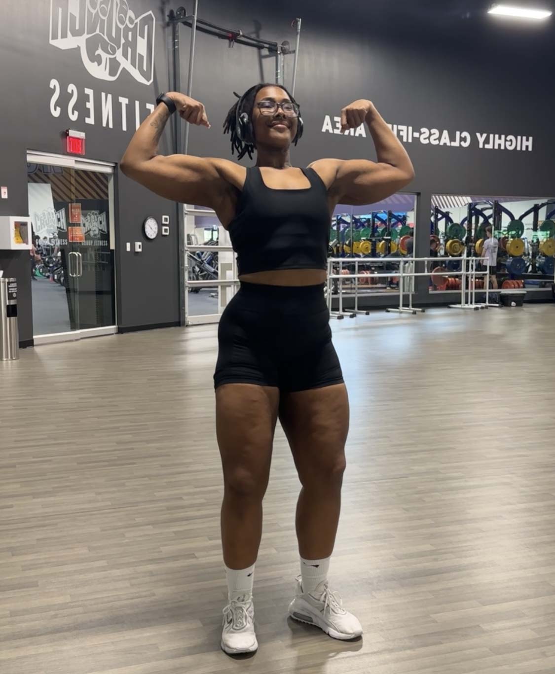 A coach stands straight, stretching both arms out to display her arm muscles.